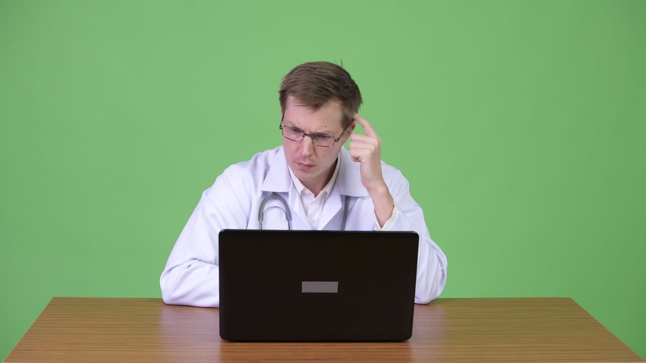 Portrait Of Young Man Doctor Sitting And Using Laptop Computer While Thinking