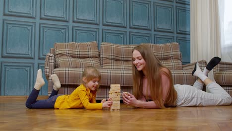 happy young mother woman teaching small child daughter playing wooden blocks board game at home