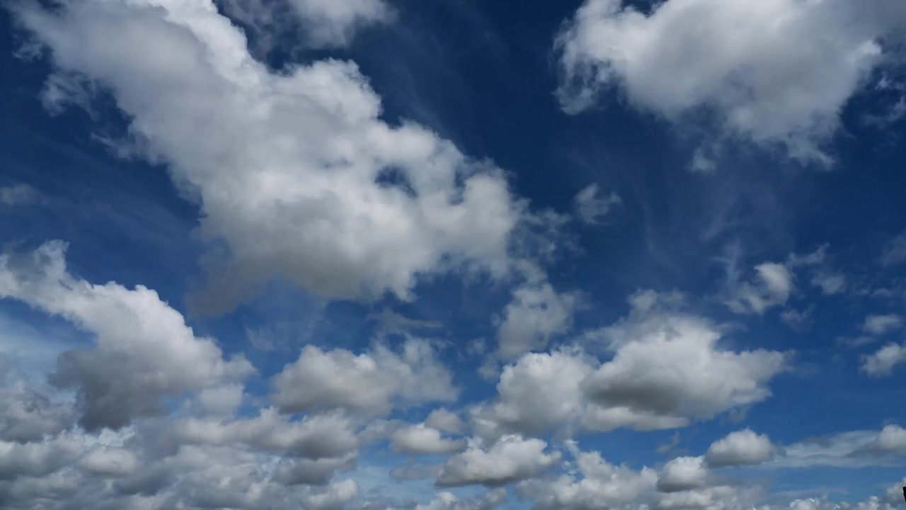 Timelapse of clouds white and grey appearing and disappearing against a blue sky.