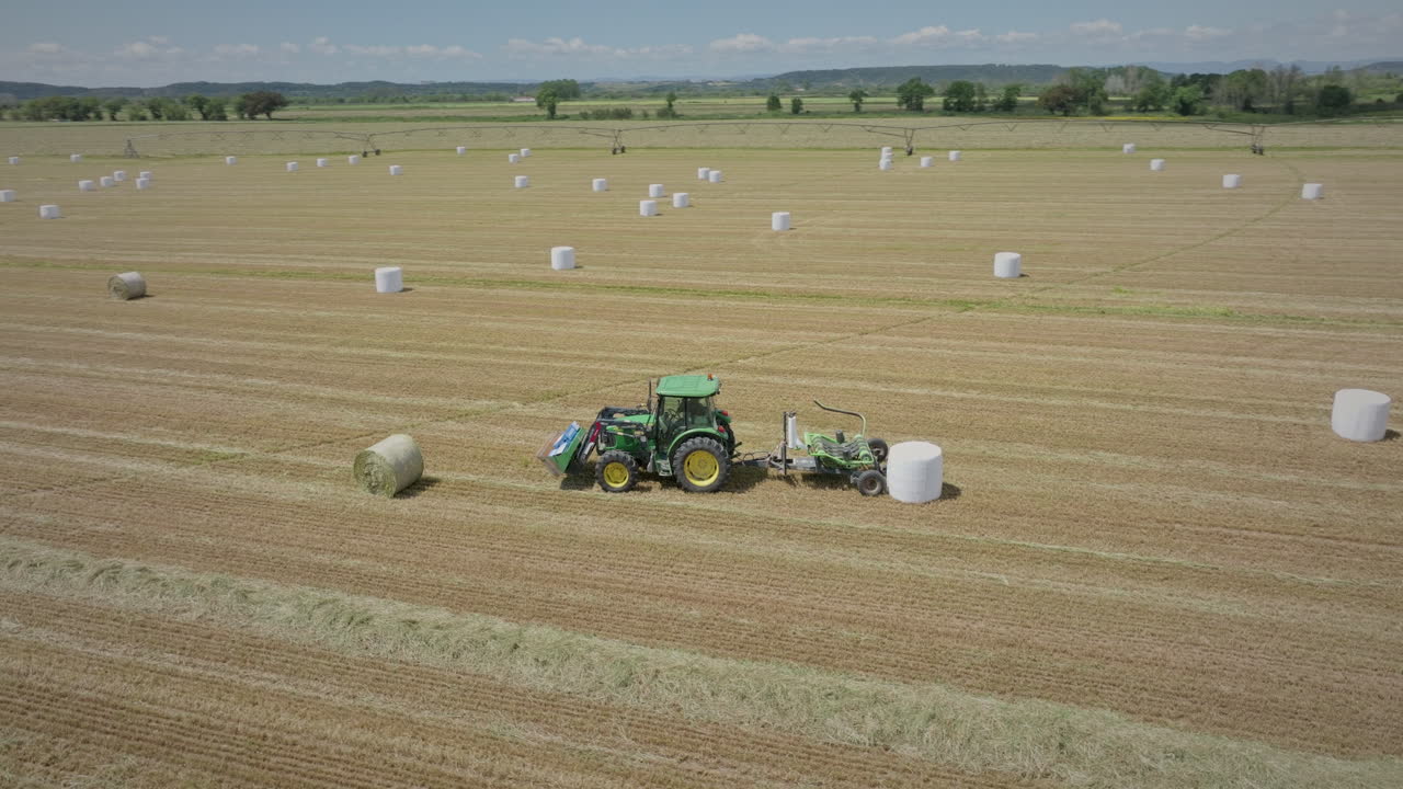 трактор на сельскохозяйственном поле обматывает тюки соломы длинный аэроснимок