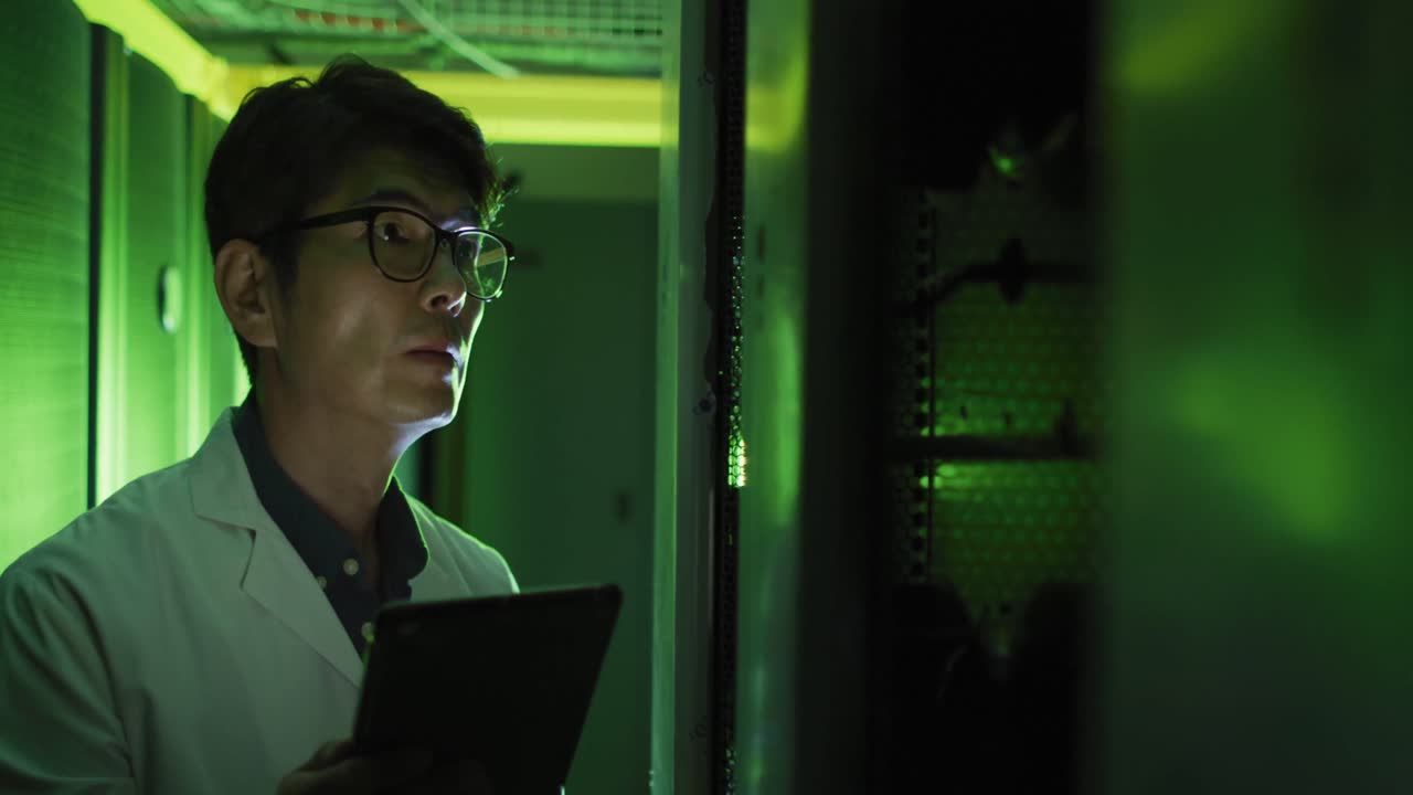 Asian male it technician in lab coat using tablet checking computer server