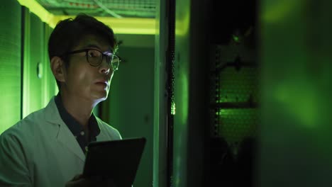 asian male it technician in lab coat using tablet checking computer server