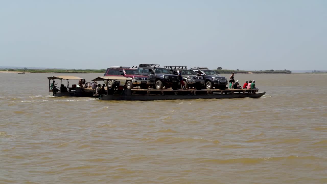 River ferry carries vehicles and people along the Tsiribihina River in Madagascar. Wide shot passing by