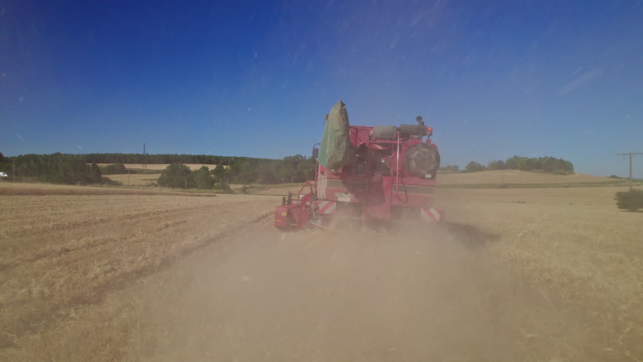 Low angle aerial shot tracking forward and closing in on a combine harvester harvesting wheat. REC709, UHD, 23,976 fps