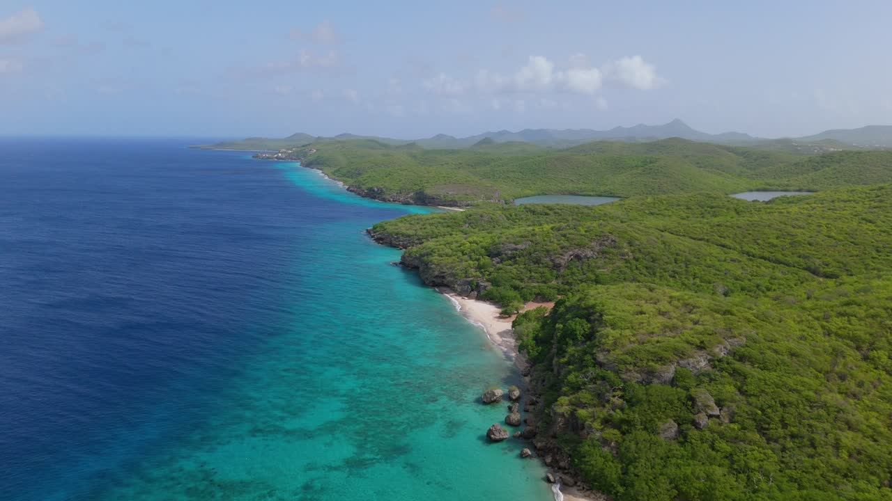 Aerial panoramic establishing of white sandy beach on stunning coastline of San Juan Beach, Curacao, vibrant turquoise waters meet sandy shore with lush surroundings