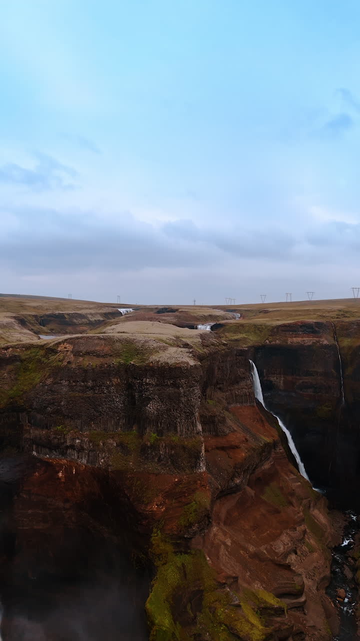 Splendid waterfalls fall from the steep rocks. Aerial perspective on the stunning nature of Iceland. Vertical video.