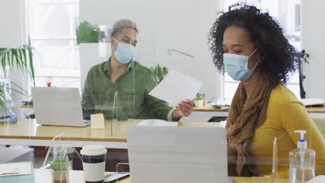 man wearing face mask passing a document to his colleague at office