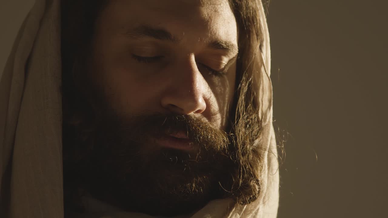 retrato de un hombre vestido con túnicas con cabello largo y barba que representa la figura de jesucristo con los ojos cerrados orando