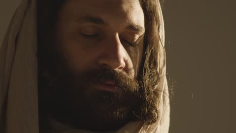 portrait of man wearing robes with long hair and beard representing figure of jesus christ with eyes closed praying