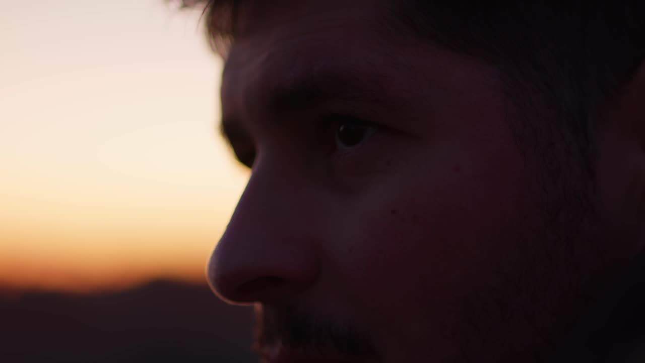 un primer plano del rostro de un hombre, mirando a la distancia con una expresión triste, mientras un cielo oscuro crea un telón de fondo dramático y emocional.