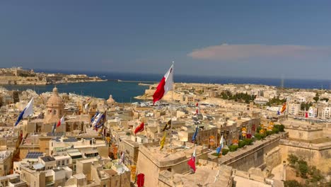 drone shot pan of malta's flag flapping amongst others in birgu fest