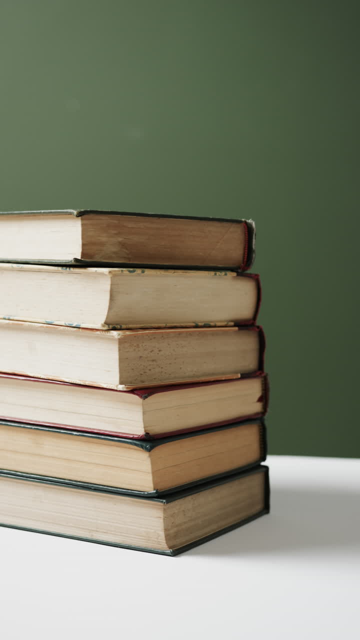 Vertical video of stack of books with copy space on green background, in slow motion
