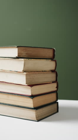 vertical video of stack of books with copy space on green background, in slow motion