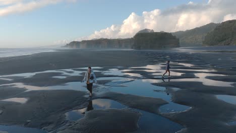 young people strolling on wet sandy shore at three sisters beach in tongaporutu, new zealand