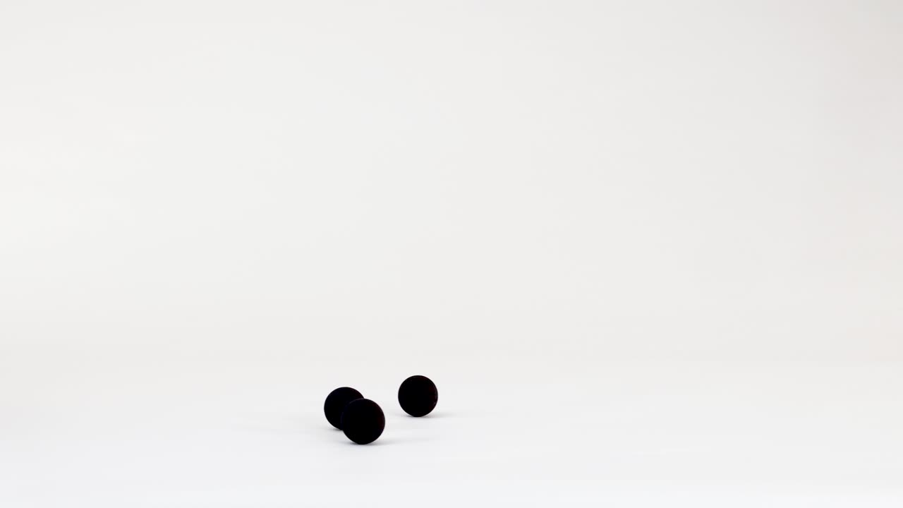 Black spheres drop and bounce across a clean white studio background with minimalist physics motion