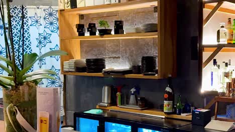 close-up of bar shelves featuring neatly arranged bottles, glassware, and a decorative plant in a vibrant setting.