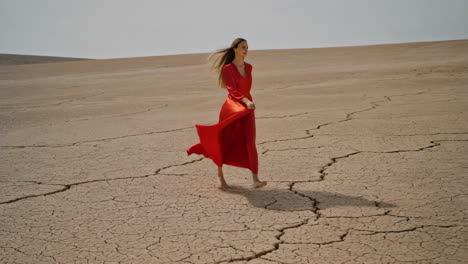 woman in flowing red dress walks through a vast cracked desert