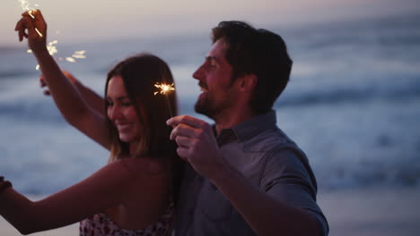 Couple,-sparkler-and-having-fun-on-the-beach