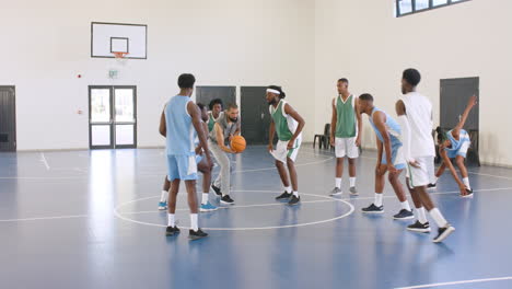 Multiracial male basketball players with multiracial male coach beginning game, running in gym