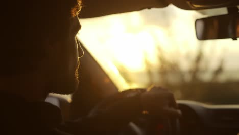 Close-up-footage-of-a-bearded-smiling-man-driving-a-car-along-the-coast,-golden-hour