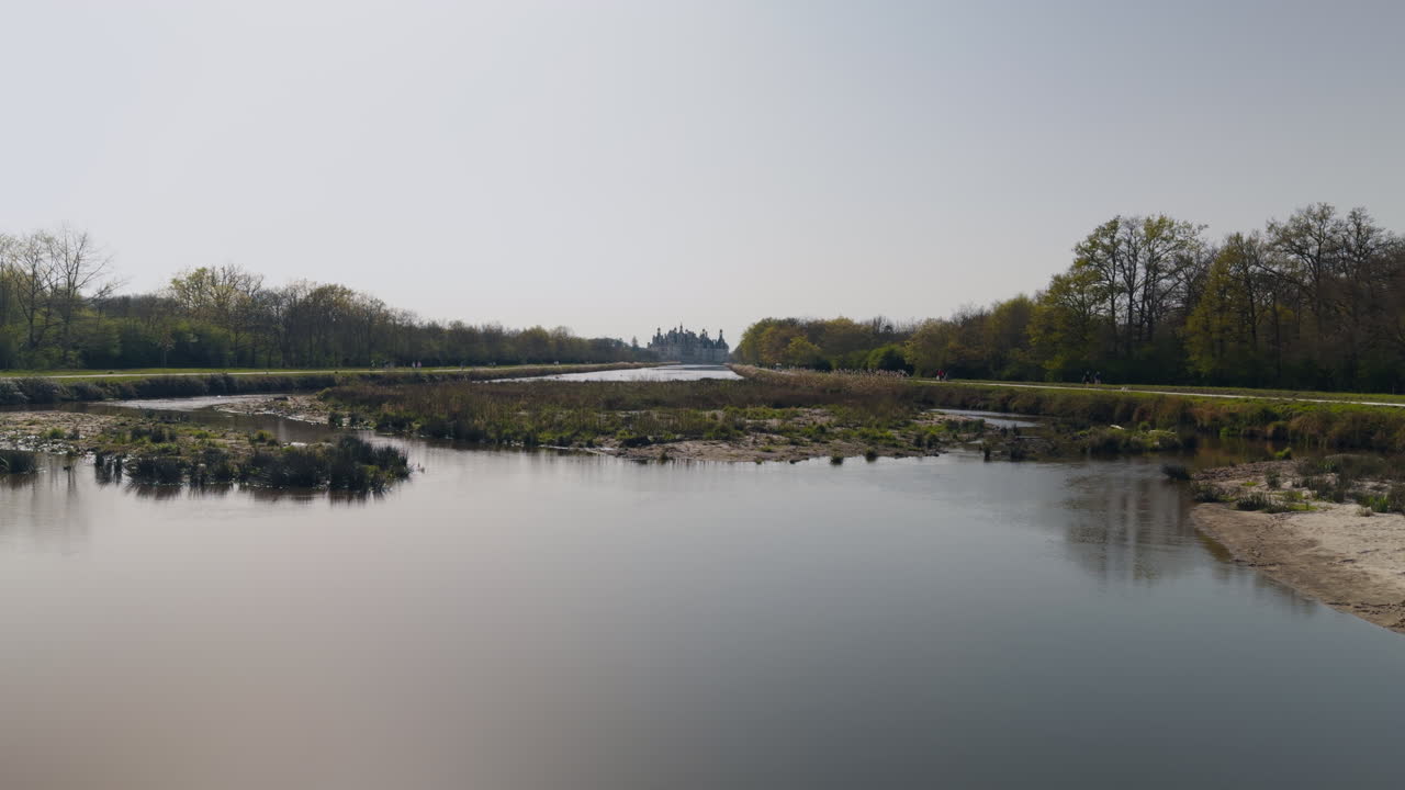 Majestic view of Chambord castle and canal with tourists near the Cosson river