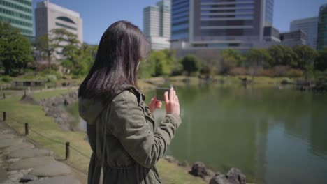 Amplia-Vista-De-Una-Hermosa-Joven-Tomando-Fotos-Con-Su-Teléfono-Inteligente-En-Un-Día-Soleado-En-Tokio,-Japón---Cámara-Lenta