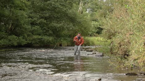 Freihandaufnahme-Eines-Fliegenfischers,-Der-Den-Fluss-Hinunterwatet-Und-Auswirft