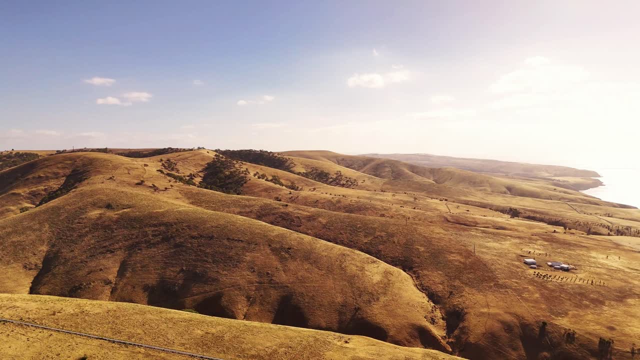 Un amplio panorama aéreo revela ondulantes colinas áridas que se extienden hacia el horizonte, estableciendo un paisaje australiano