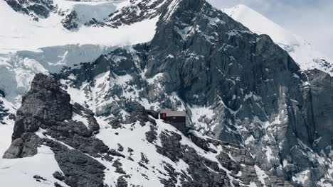 descending circling right shot of alpine hut with glacier and snow-covered peaks