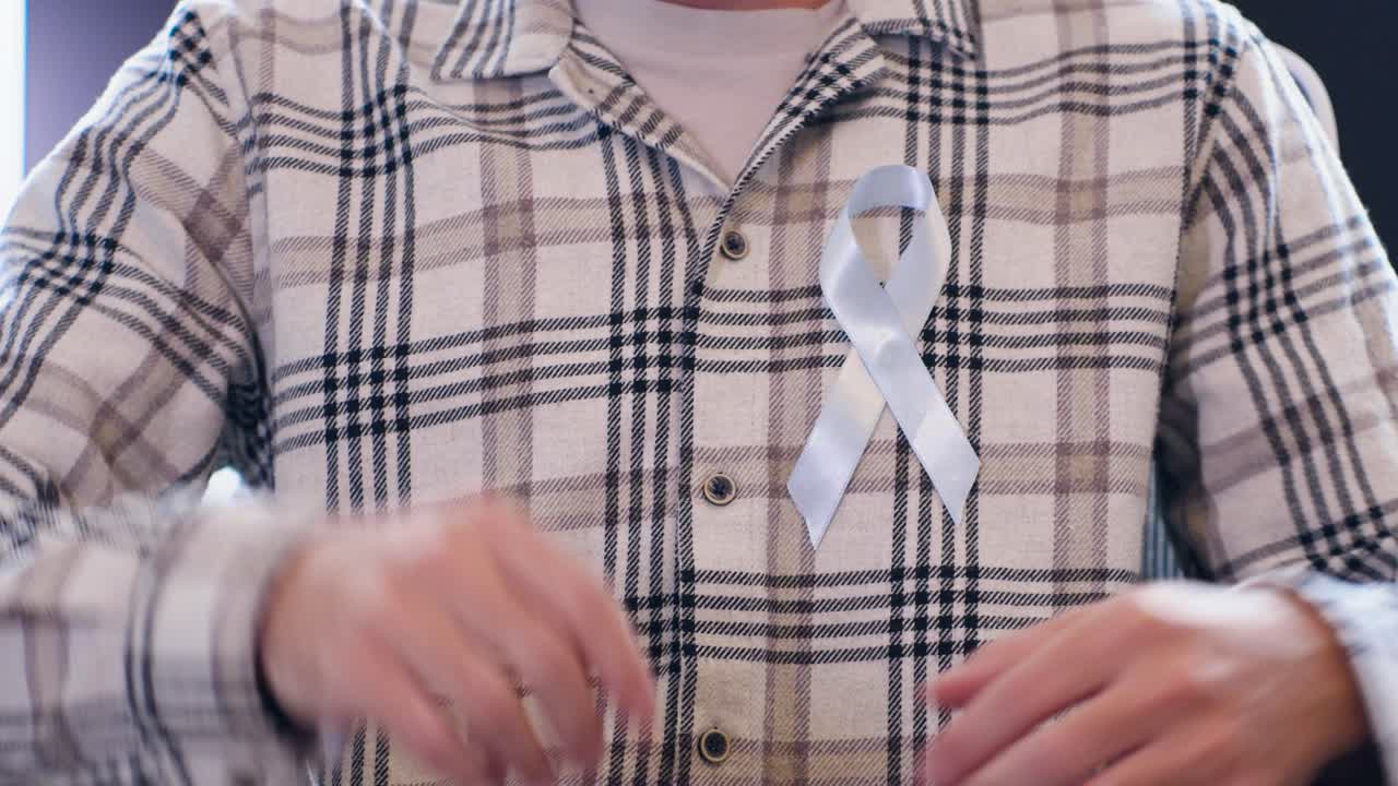 Ritratto di un uomo sorridente che attacca un nastro blu alla camicia in supporto di Movember e della sensibilizzazione sul cancro alla prostata. Concept di salute maschile e campagna di prevenzione