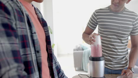 una feliz pareja de hombres homosexuales preparando un batido de frutas saludable en la cocina, en cámara lenta.