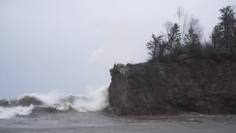 Slow-motion-of-rough-stormy-waves-crashing-against-rock-cliff-on-gloomy-day