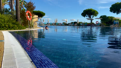 Waterfront-of-big-luxury-swimming-pool-daytime,-lounge-with-Umbrellas-and-deckchairs-on-background-in-Andalusia,-Spain,-stone-pine-trees