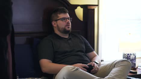 el hombre se ríe y trata de concentrarse en un videojuego mientras sus amigos hablan y caminan por la habitación