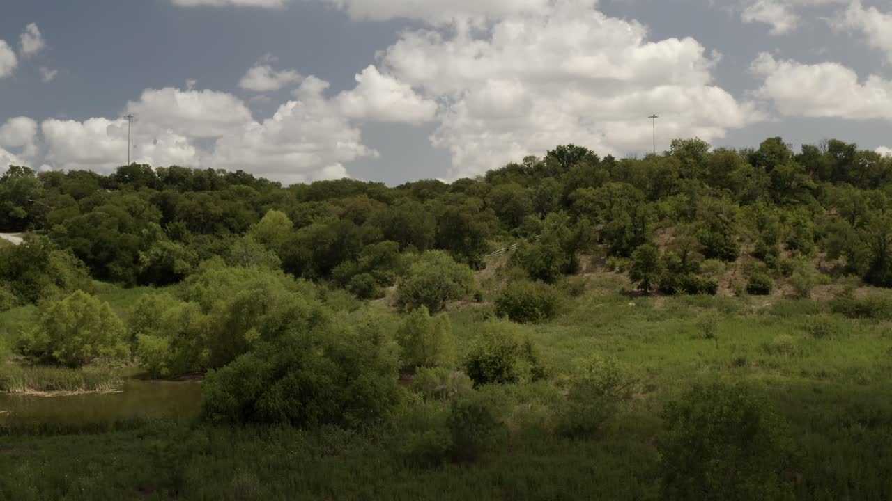 una nube arriba se mueve y revela un cielo azul, nubes blancas con árboles verdes y hierba junto a un estanque