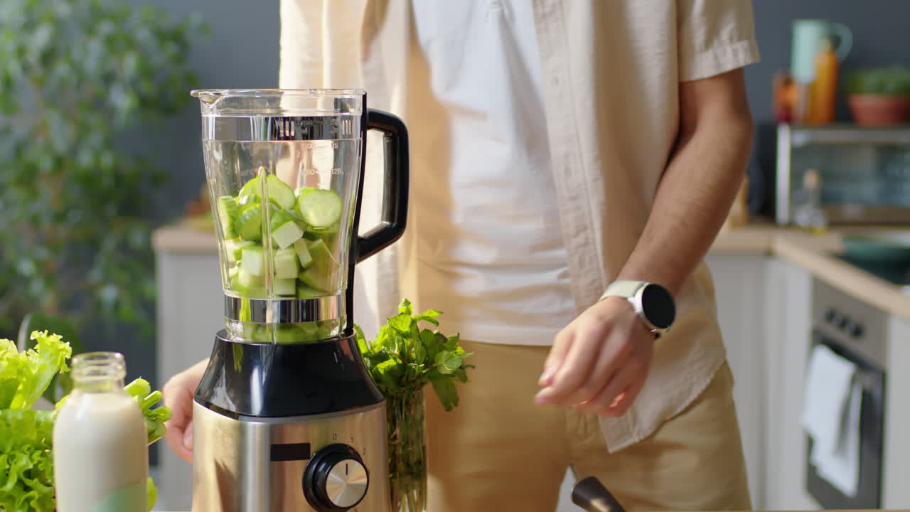 Man Putting Fresh Cucumber in Kitchen Blender