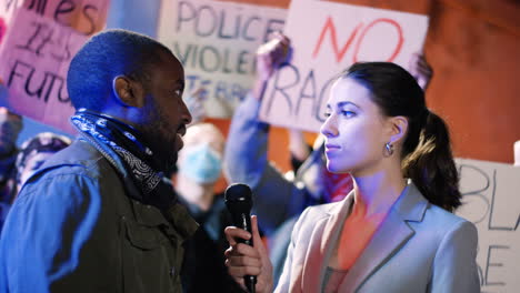 african american man agitatedly answering female interviewer's questions in a manifestation against racism with group of multi-ethnic people