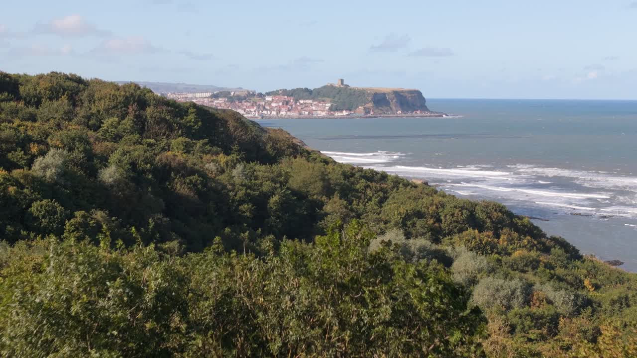 aerial drone footage of Scarborough taken from a distance away over Cayton Bay with blue sky and ocean and big waves