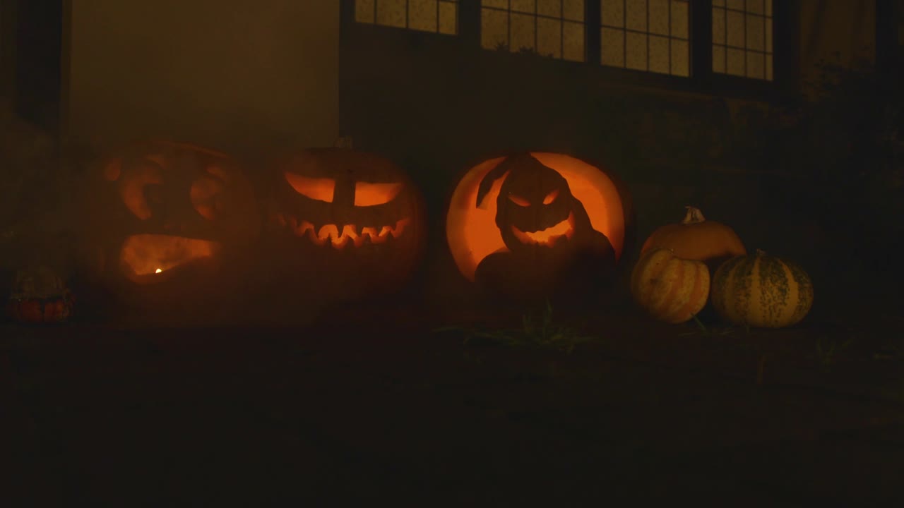 3 carved lit pumpkins outside the front of a house Halloween with smoke