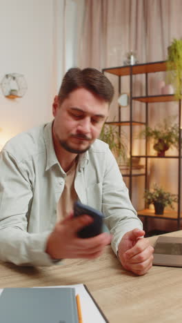 upset displeased man freelancer using smartphone reading bad news sitting at table in living room