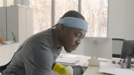 cleaning man wearing bandana and uniform cleaning a desk inside an office