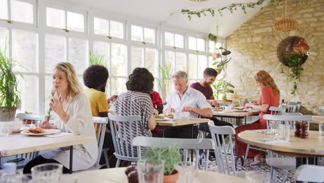 Customers-sitting-at-tables-in-a-busy-restaurant-eating,-daytime,-general-view