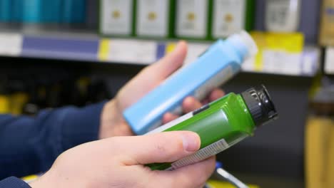 a man holds two shower gels in his hands, reads the composition and chooses the best one for himself. shopping for toiletries in a supermarket, a man chooses a shampoo and lays down a purchase