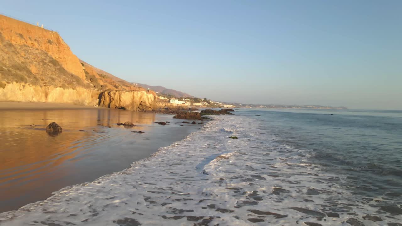 Beautiful view of waves rolling from the Pacific Ocean into the shore and people walking on the sand at El Matador Beach during golden hour, Malibu California