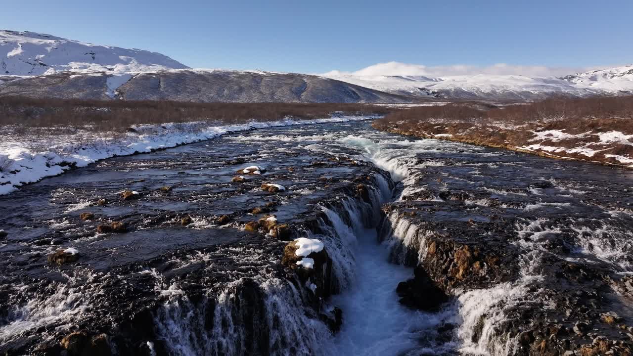Waterfall cascading through rocky terrain surrounded by snowy mountains in Iceland