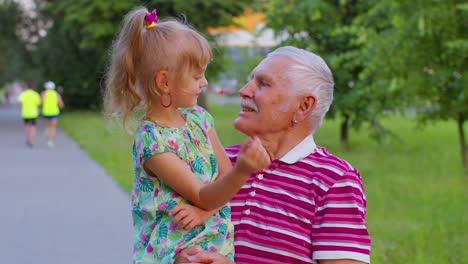 little granddaughter child embracing kissing with her grandfather in park, happy family relationship