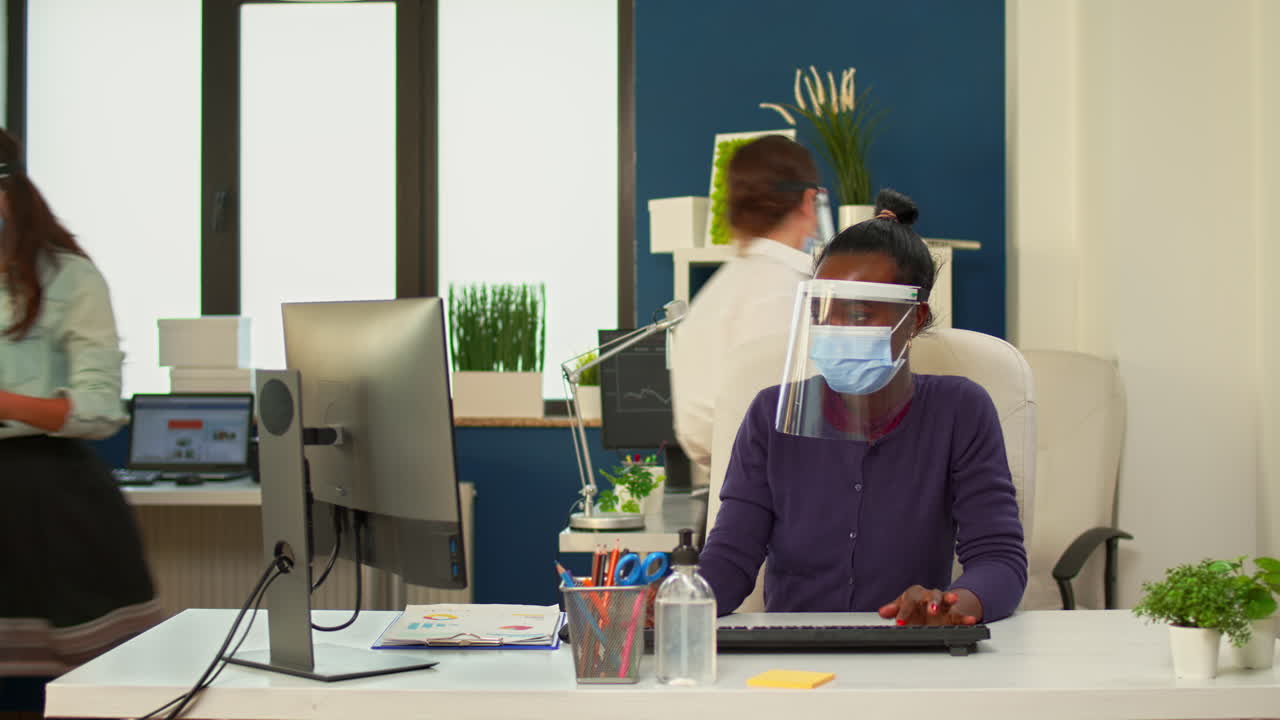 마스크를 쓴 아프리카의 사업가 여성이 컴퓨터로 보고서를 쓰고 있습니다.