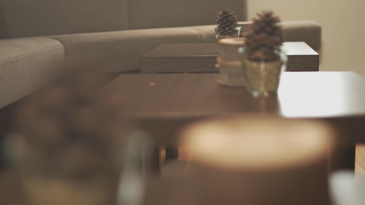 Modern design wooden candle and a pinecone on a table in a hotel lobby with a wooden table with another candle and a pinecone in the background