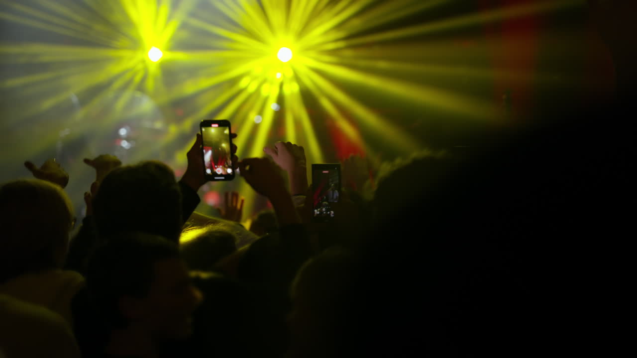Folla a un concerto che riprende una performance dal vivo con smartphone e luci intense del palco