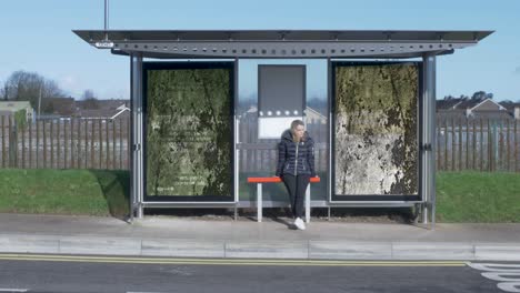 attractive young woman waits for the bus at a bus stop sitting